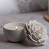 White ceramic rose next to a lit candle in a bowl on a marble surface.